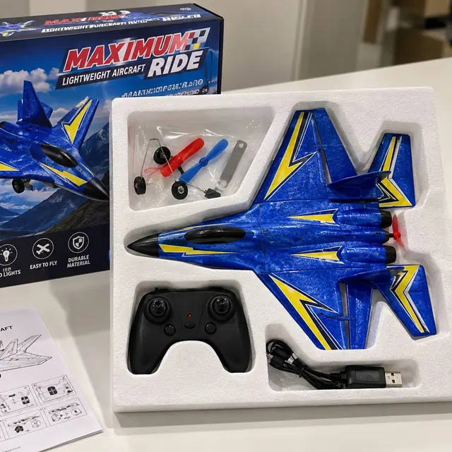 Caja abierta con el avión teledirigido azul, el mando, el cable USB, las hélices y la hoja de instrucciones